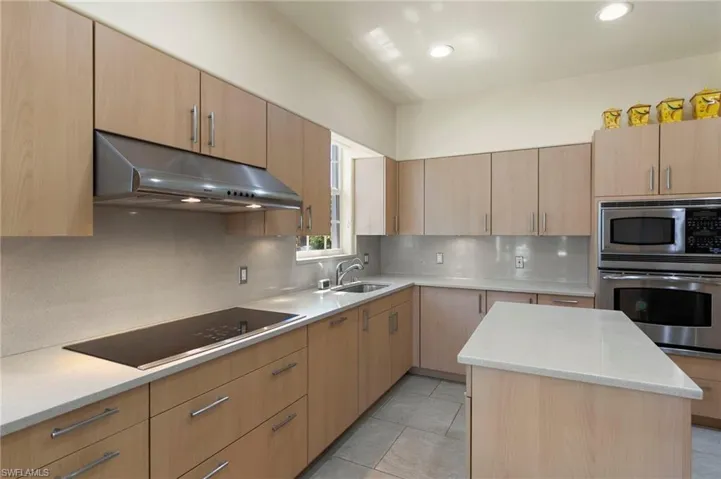 Well-appointed kitchen featuring light wood-finish cabinetry, light-toned countertops, and a full suite of stainless steel appliances including a built-in oven and microwave