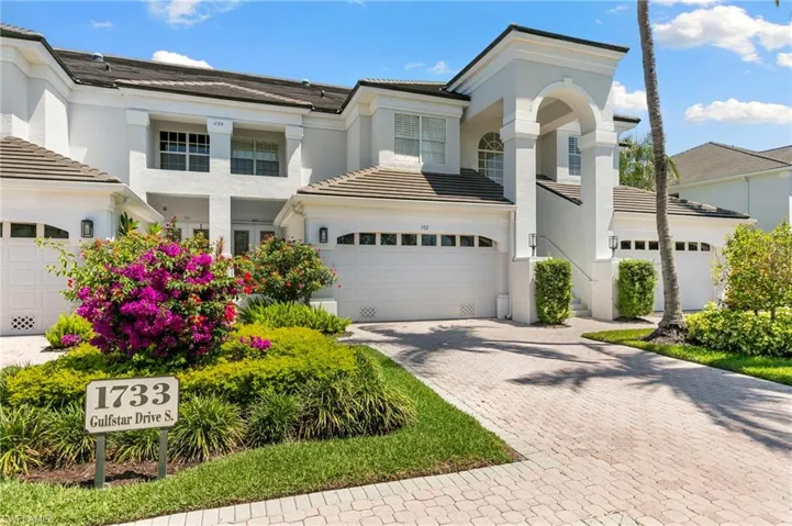 Contemporary stucco exterior with arched entryways, tile roofing, private garage, paver driveway, and mature landscaping