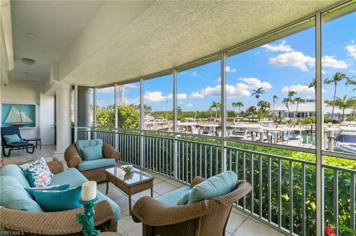 Screened-in balcony with a marina backdrop, featuring white pillars, tile flooring, and a metal railing