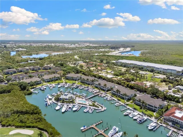 Waterfront community featuring multiple buildings, a central marina with numerous boat slips, and surrounding lush green landscaping