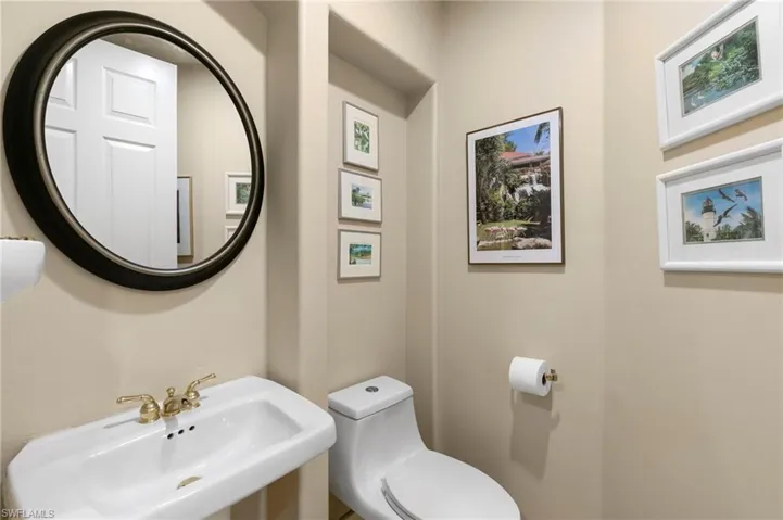 Pedestal sink with brass-finish faucet, circular framed mirror, and toilet featuring a dual-flush mechanism