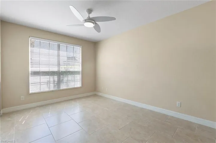 Neutral-toned room featuring a large window with horizontal blinds, a modern ceiling fan with integrated lighting, tiled flooring, and light-colored wall paint with white baseboards
