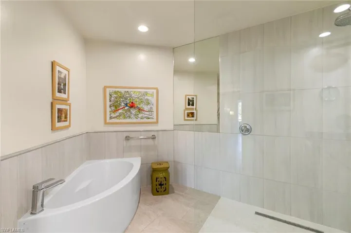 Modern bathroom featuring a freestanding soaking tub with a chrome faucet, a glass-enclosed shower with a linear drain, large format wall tiling, recessed lighting, and a full-height mirror