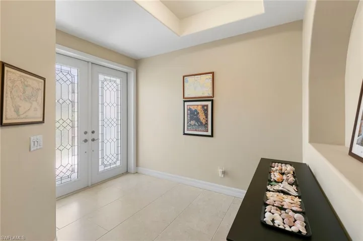 Entryway featuring double doors with decorative glass panels, recessed ceiling detail, light-toned tile flooring, and neutral wall tones