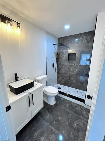 Bathroom featuring vanity, a tile shower, and toilet