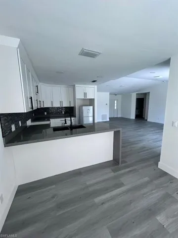 Kitchen with white cabinetry, dark hardwood / wood-style floors, kitchen peninsula, white fridge, and decorative backsplash