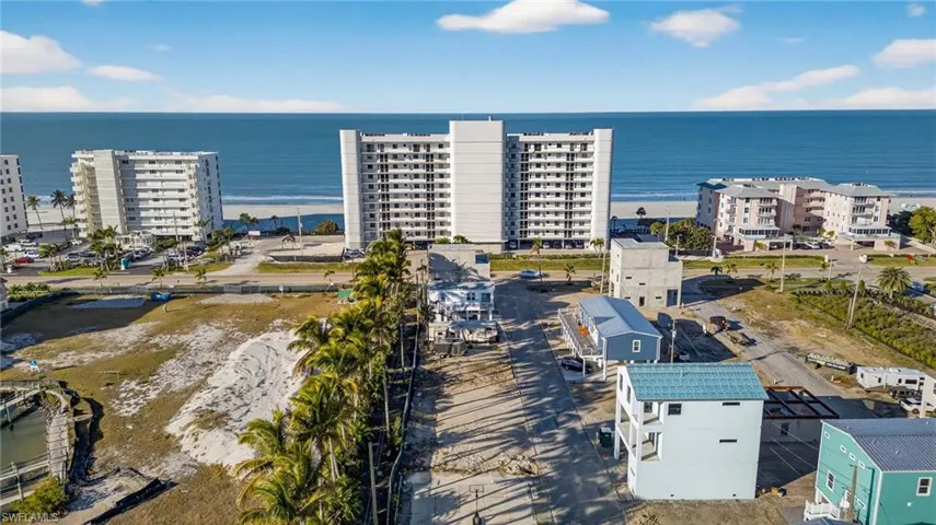 Aerial perspective of coastal property featuring proximity to shoreline, mature palm trees, paved access, and multi-level structural architecture