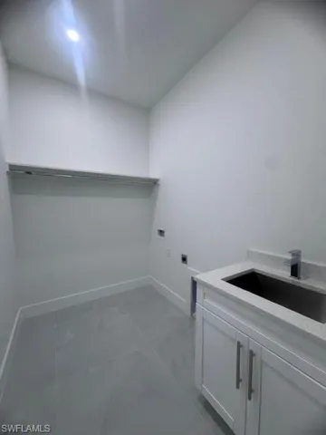 Utility room featuring light grey flooring, white cabinetry with silver hardware, a square undermount sink, and a quartz countertop