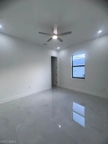 Spacious room featuring polished tile flooring, a modern ceiling fan with integrated lighting, recessed ceiling lights, a tall baseboard, and a window with a dark frame