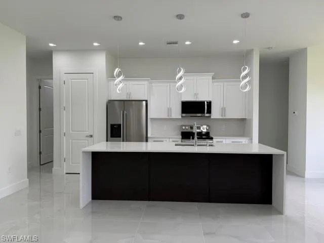 Contemporary kitchen featuring a large island with a light-toned countertop, white cabinetry, stainless steel appliances, and sleek pendant lighting