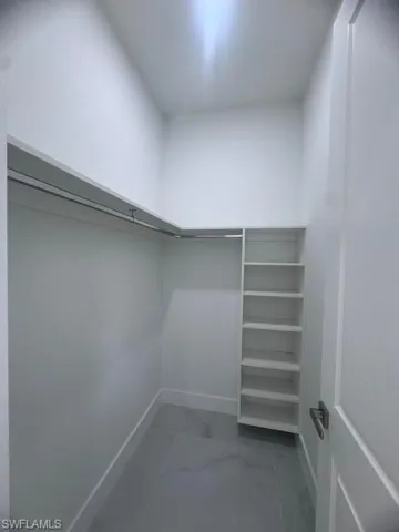 Walk-in closet featuring white walls, gray tile flooring, a built-in shelving unit, and a metal hanging rod system