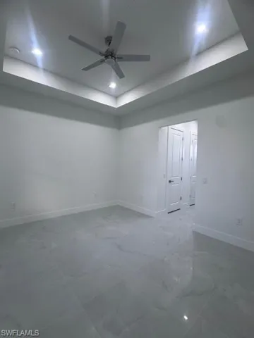 Spacious room featuring a tray ceiling with recessed lighting and a ceiling fan