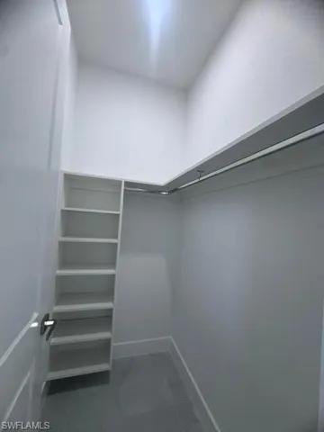 Walk-in closet featuring built-in shelving, chrome hanging rods, and gray tile flooring