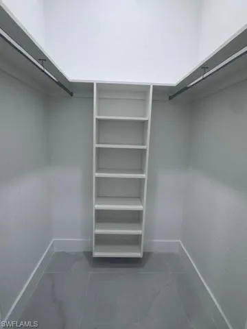 Walk-in closet featuring built-in shelving, dual hanging rods, light gray walls, and large format grey tile flooring