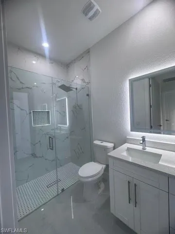 Glass-enclosed shower with large format marble-look tile, rainfall showerhead, and mosaic tile pan