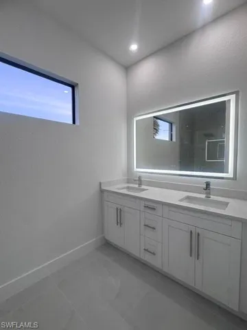 Bathroom featuring a dual vanity with white shaker-style cabinetry, chrome hardware, undermount sinks, and a light-toned countertop
