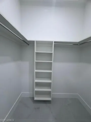Walk-in closet featuring built-in shelving, hanging rods, and large format grey tile flooring