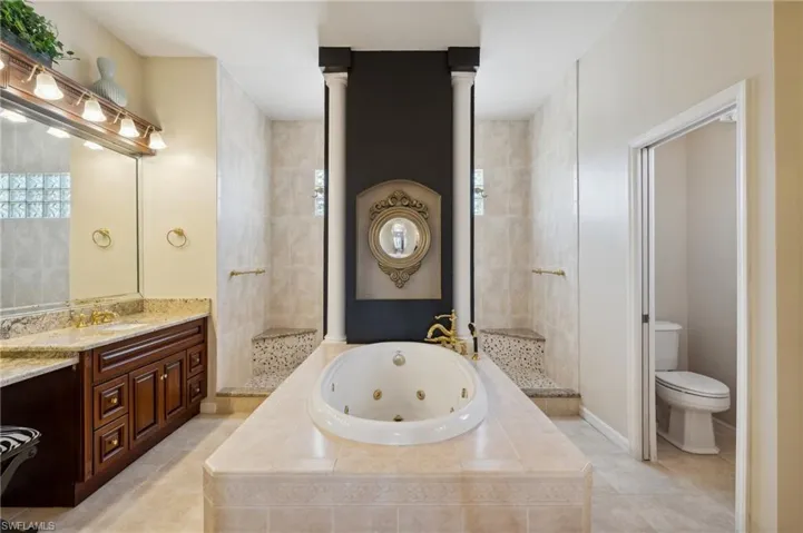 Bathroom with vanity, decorative columns, tiled bath, tile patterned floors, and toilet