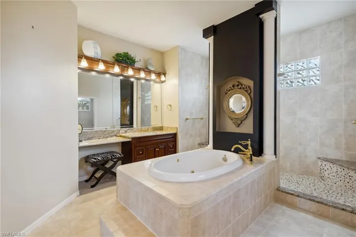 Bathroom with tile patterned flooring, vanity, tiled tub, and decorative columns