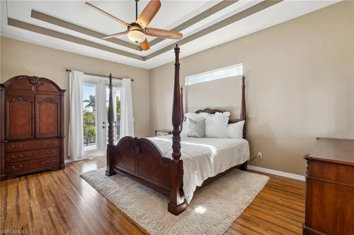 Bedroom featuring access to outside, a tray ceiling, wood-type flooring, and ceiling fan
