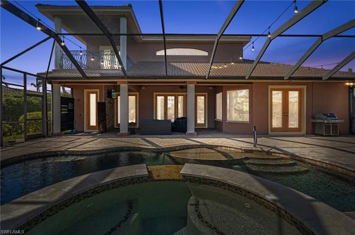 Back house at dusk featuring glass enclosure, french doors, a patio area, a pool with hot tub, and ceiling fan
