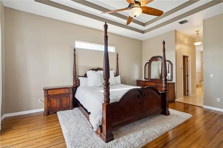 Bedroom with hardwood / wood-style flooring, ceiling fan, and a raised ceiling