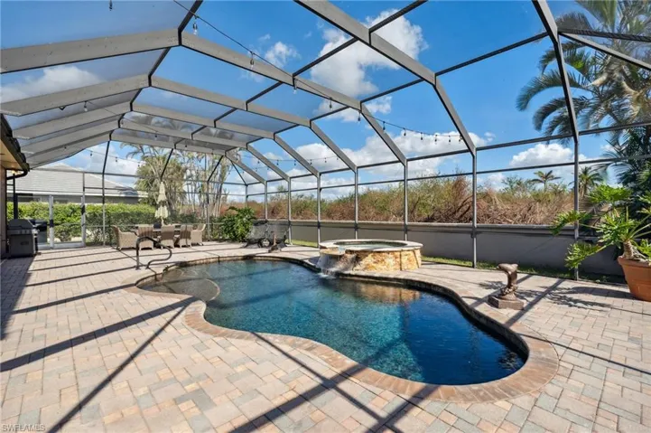 View of pool featuring glass enclosure, a patio area, grilling area, and an in ground hot tub