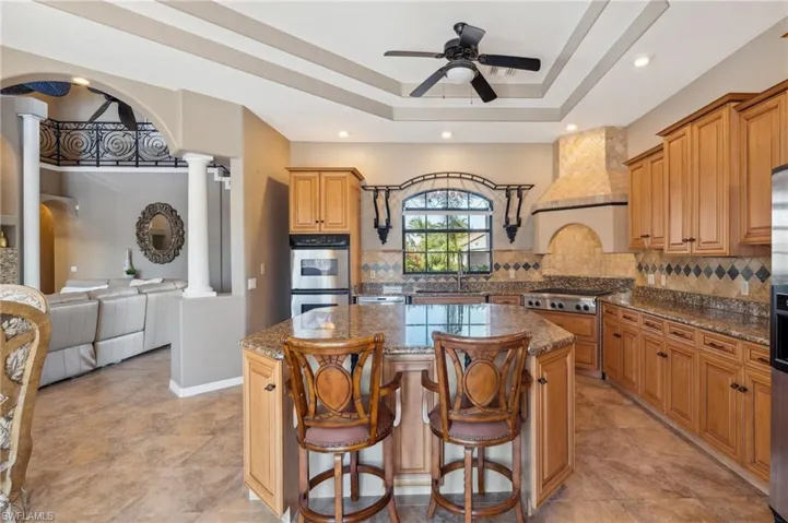 Kitchen featuring appliances with stainless steel finishes, backsplash, stone counters, decorative columns, and a center island