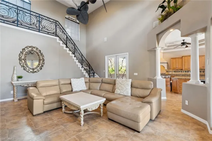 Tiled living room with ornate columns, ceiling fan, and a high ceiling