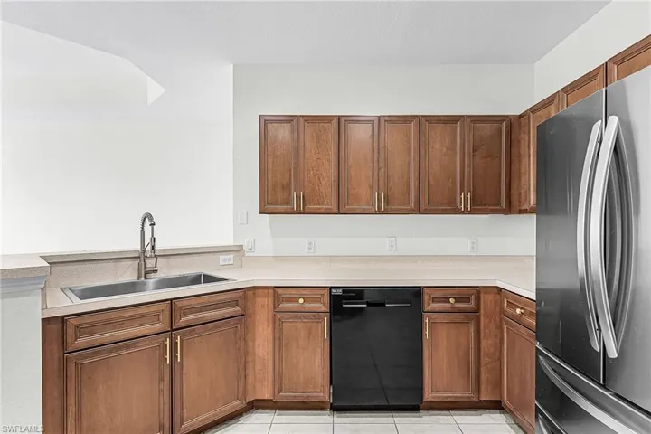 Kitchen with freestanding refrigerator, dishwasher, light countertops, light tile patterned floors, and wood finish cabinets