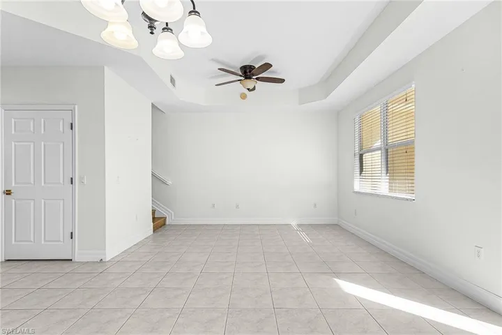 Unfurnished room featuring a ceiling fan, hanging lights, light tile patterned flooring, and a tray ceiling