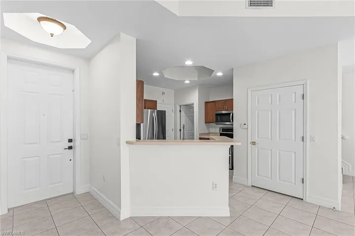 Kitchen with wood finish cabinetry, light countertops, stainless steel appliances, a peninsula, and light tile patterned flooring