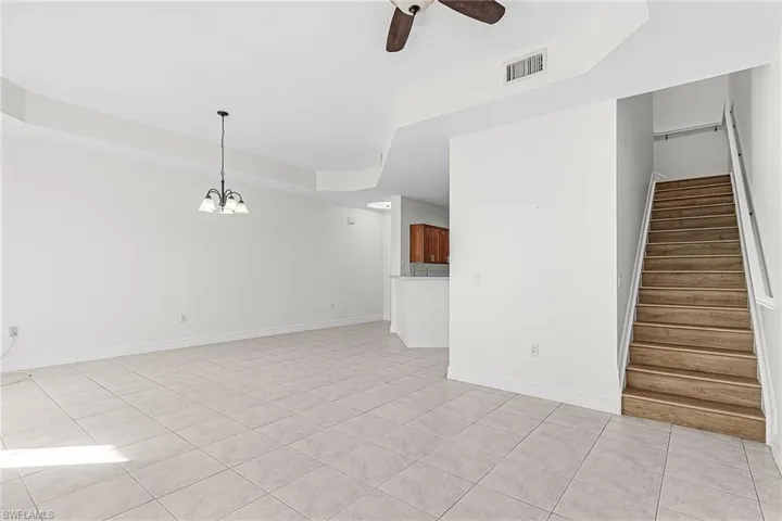 Unfurnished living room with a tray ceiling, ceiling fan, hanging lights, and light tile patterned flooring