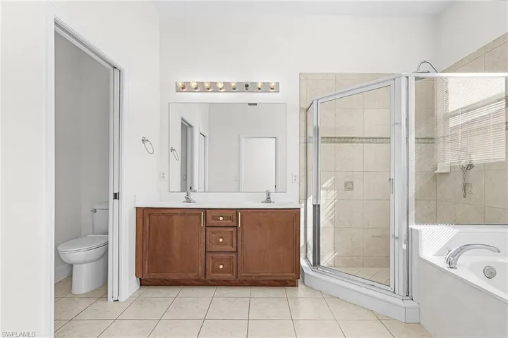 Bathroom featuring a garden tub, a stall shower, double vanity, and light tile patterned flooring