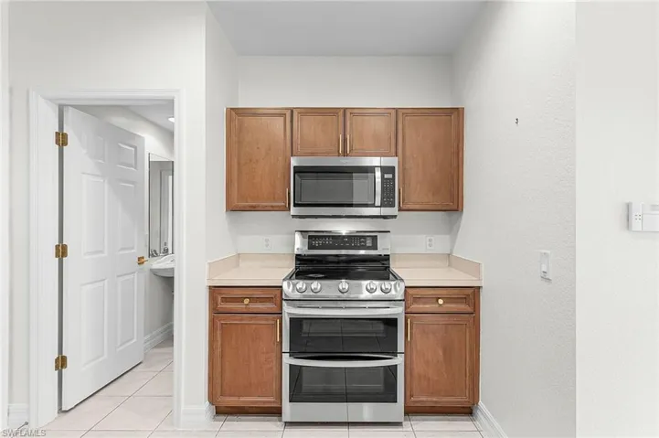 Kitchen with stainless steel appliances, wood finish cabinets, light countertops, and light tile patterned floors