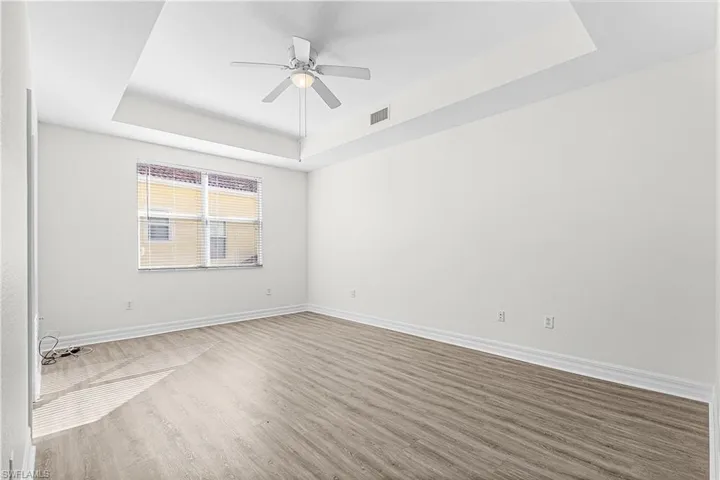 Spare room with a tray ceiling, ceiling fan, and wood finished floors