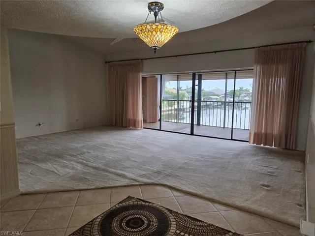 living room with carpet floors, a textured ceiling, a water view, tile patterned flooring, and vaulted ceiling