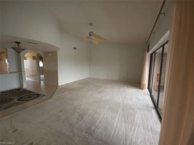 Unfurnished living room featuring arched walkways, light tile patterned flooring, ceiling fan, and light colored carpet