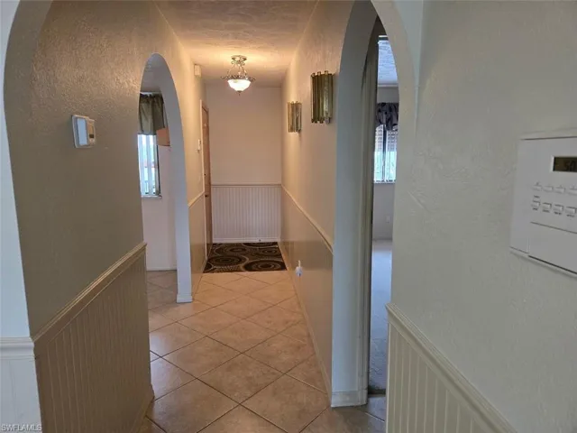 Hallway featuring wainscoting, a textured wall, light tile patterned flooring, arched walkways, and a decorative wall