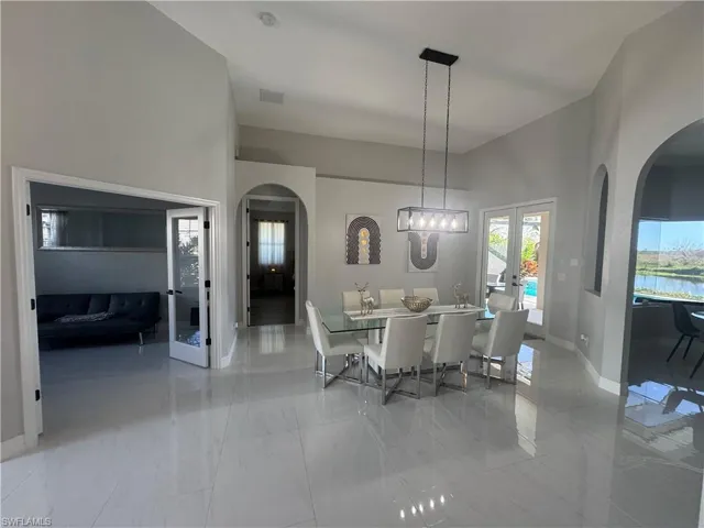 Dining space with arched walkways, french doors, a high ceiling, and light marble finish flooring