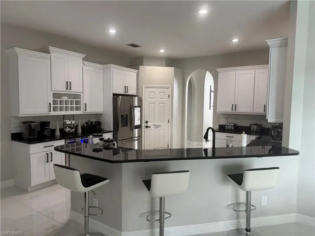 Kitchen featuring decorative backsplash, a breakfast bar area, white cabinets, stainless steel fridge, and recessed lighting
