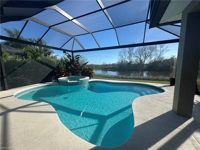 View of pool with a lanai, a pool with connected hot tub, a sunroom, a water view, and a patio area