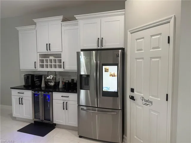 Kitchen with stainless steel refrigerator with ice dispenser, wine cooler, white cabinets, backsplash, and dark stone countertops