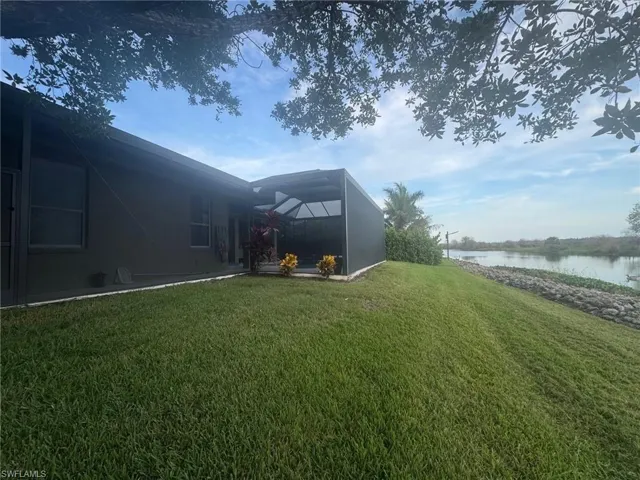 View of grassy yard featuring glass enclosure, a water view, and a sunroom