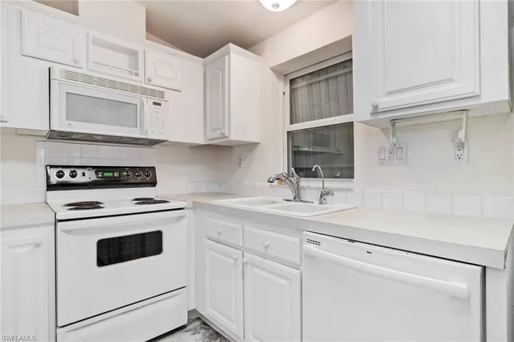 Kitchen featuring white appliances, light countertops, and white cabinetry