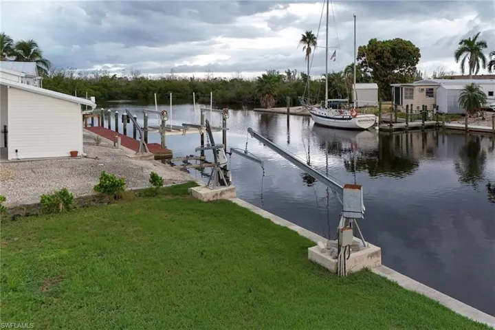Dock area with a water view, boat lift, and a lawn
