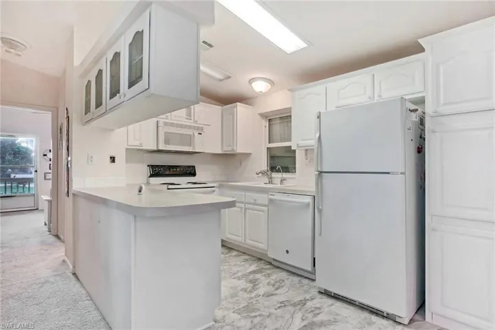 Kitchen featuring white appliances, light countertops, white cabinetry, a peninsula, and glass insert cabinets