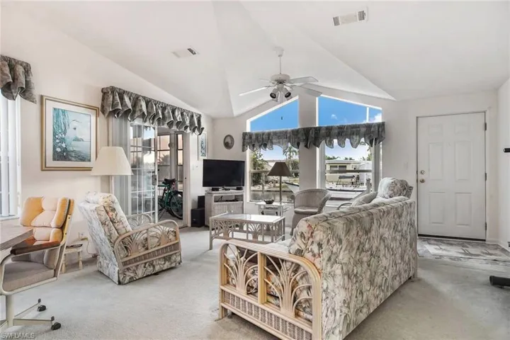Living area featuring carpet flooring, vaulted ceiling, and ceiling fan