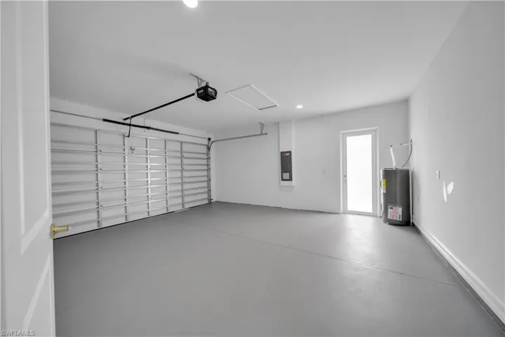 Garage with a garage door opener, water heater, electric panel, and recessed lighting