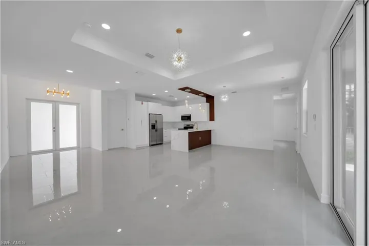 Unfurnished living room with a raised ceiling, a chandelier, recessed lighting, and baseboards